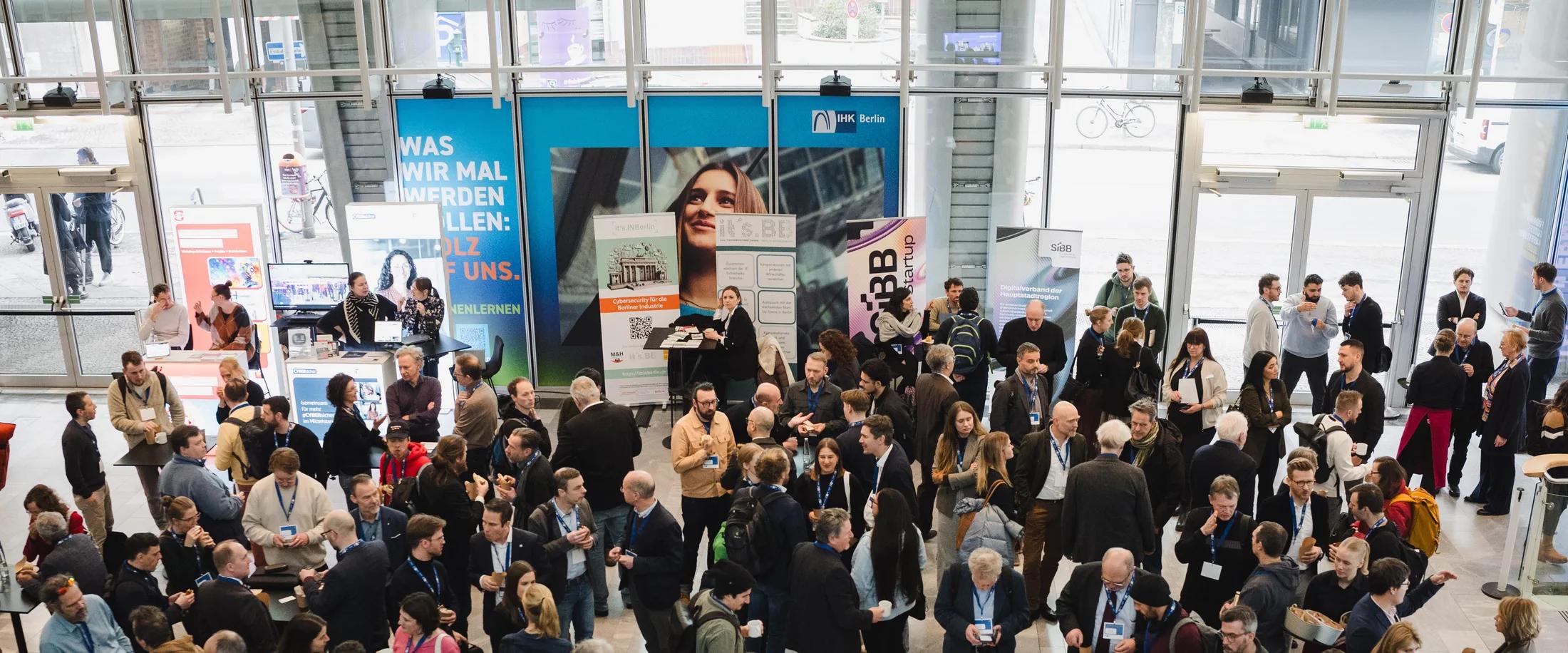 Gefülltes Foyer der IHK Berlin während der DIGITAL+-Konferenz am 10. Februar 2026 — Hunderte Teilnehmende im Gespräch zwischen den Ausstellungsbannern.