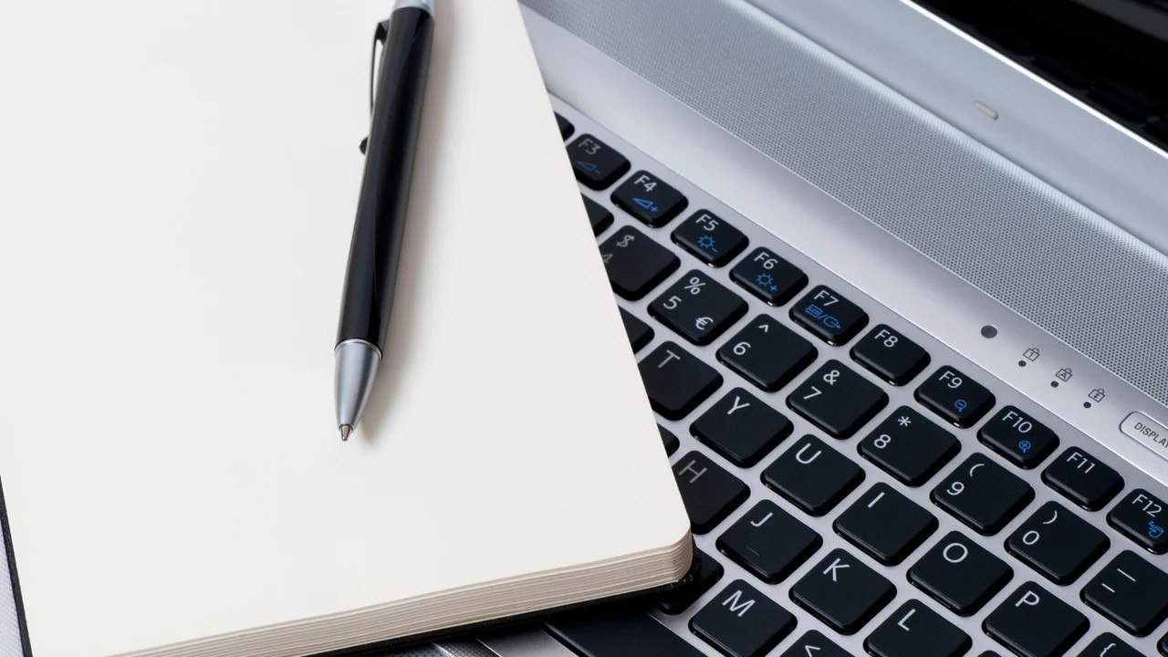 Notizbuch und Stift auf einer Laptop-Tastatur — Fallstudien-Arbeit.