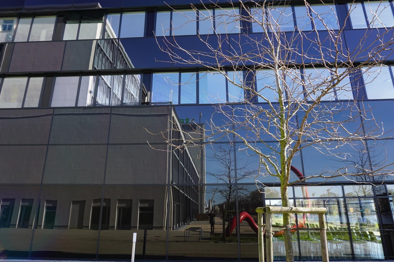 Glasfassade der HTW Berlin mit Baumspiegelung.